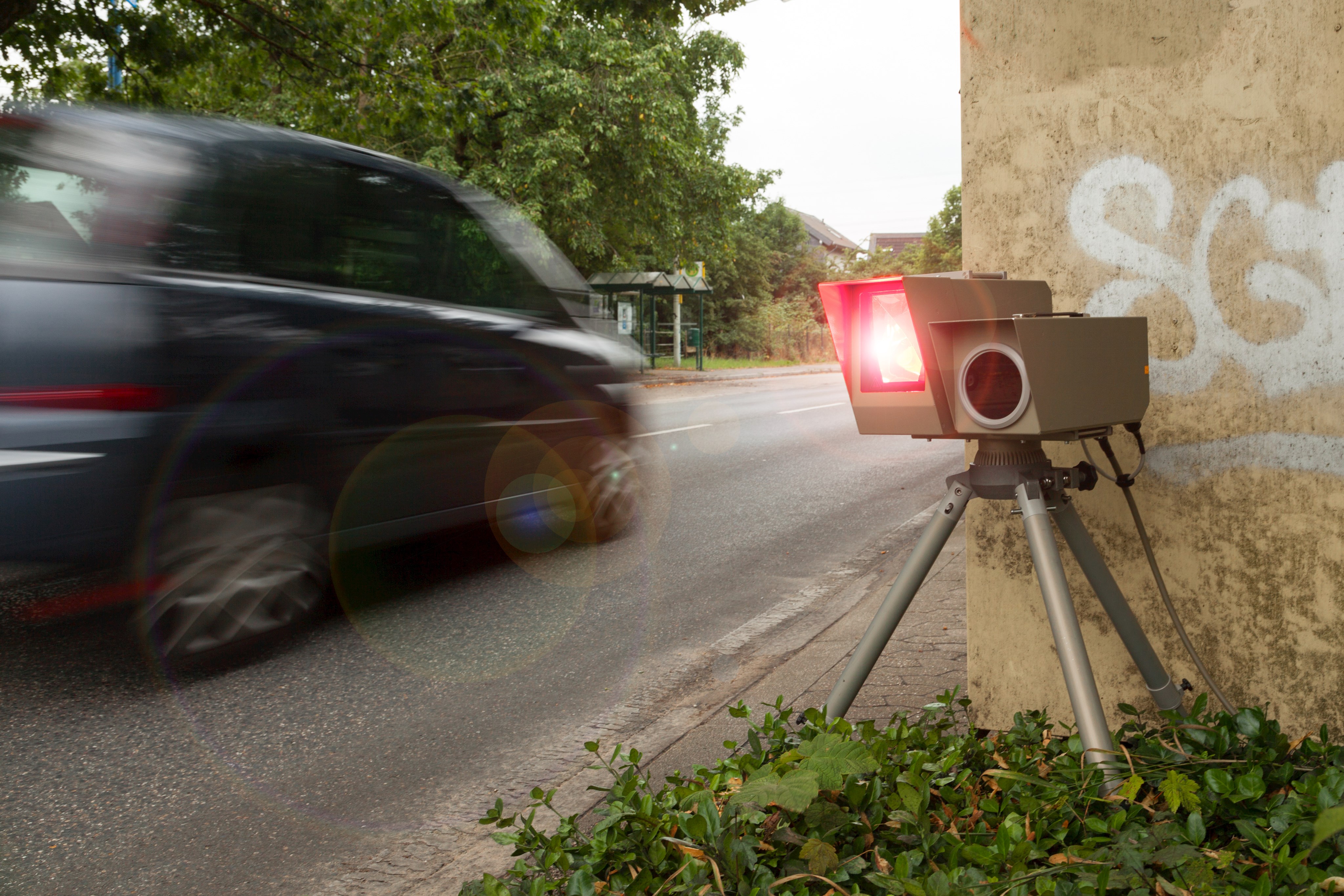 Das Bild zeigt eine auslösende Geschwindigkeitsmessanlage mit vorbeifahrendem Auto.